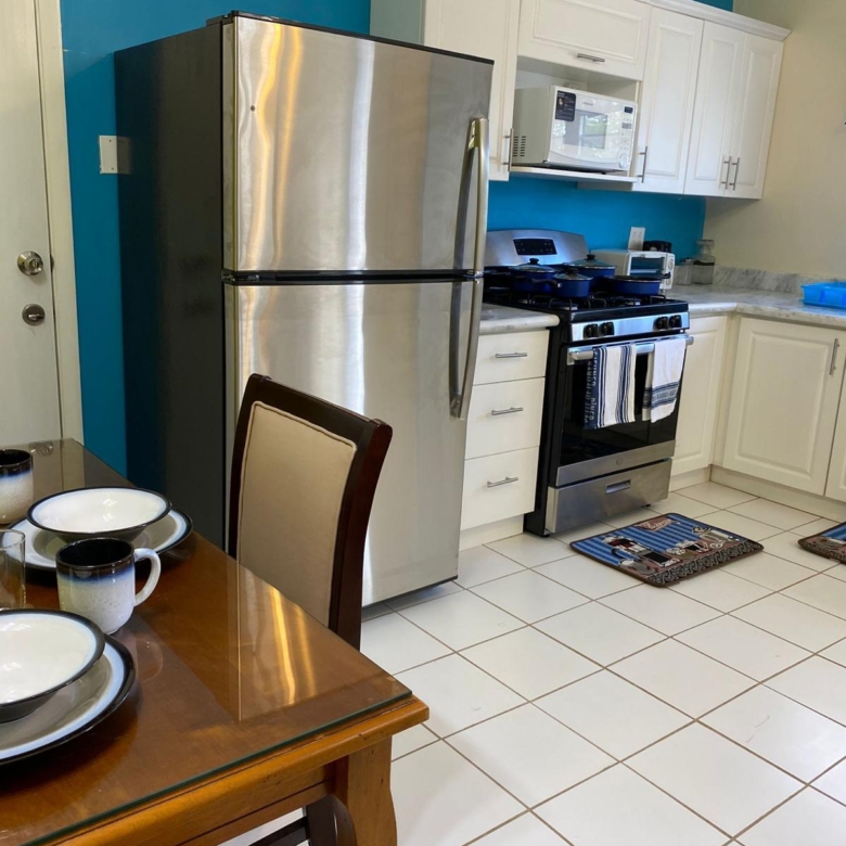 Kitchen with stainless steel refrigerator, gas range, microwave and dining table in a furnished 1 bedroom rental at Crescent Hill, St. Kitts