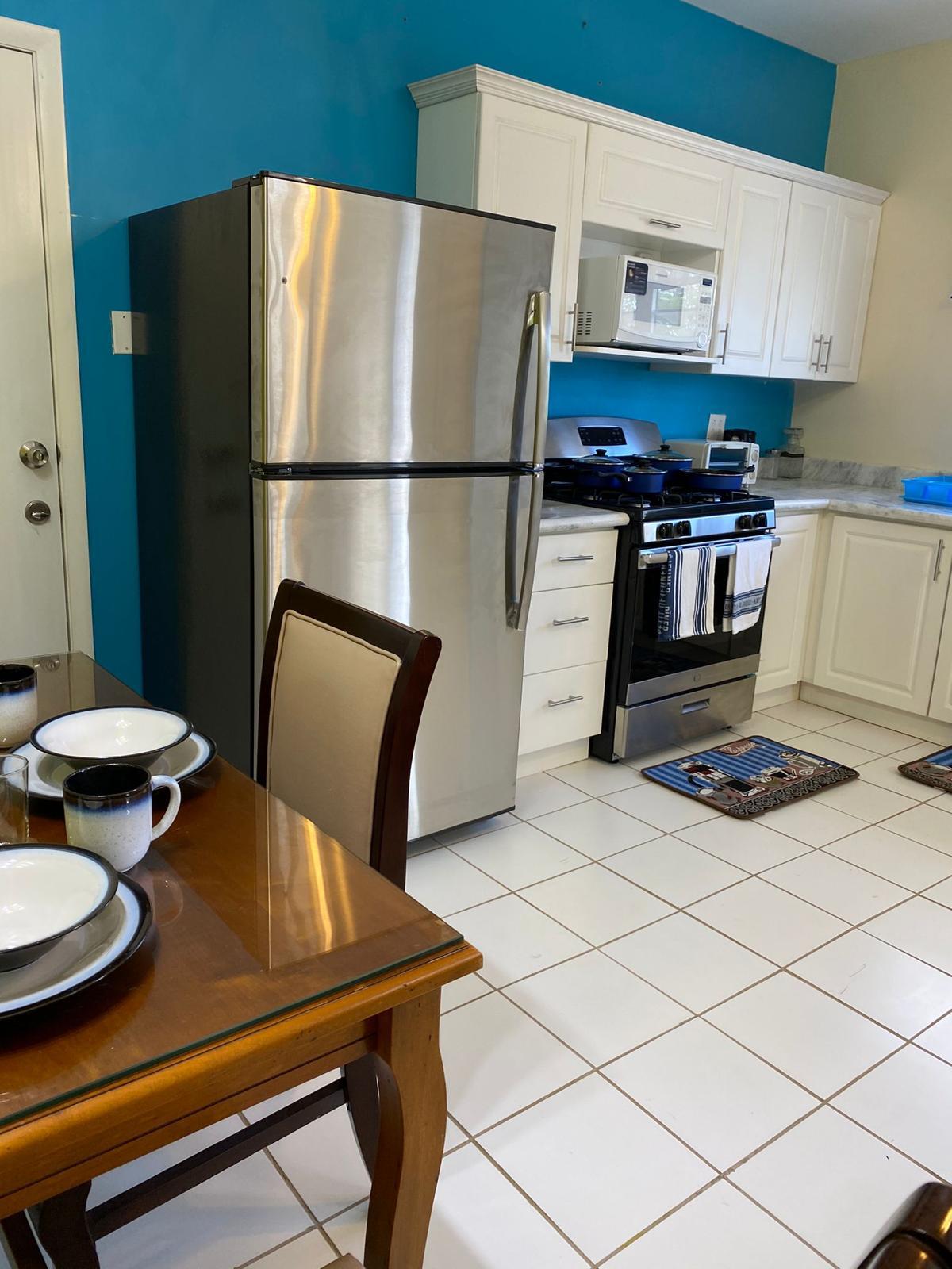 Kitchen and dining area Kitchen with stainless steel refrigerator, gas range, microwave and dining table in a furnished 1 bedroom rental at Crescent Hill, St. Kitts