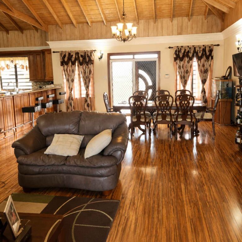 Furnished open-plan living and dining area with timber ceiling, chandelier and kitchen bar beyond