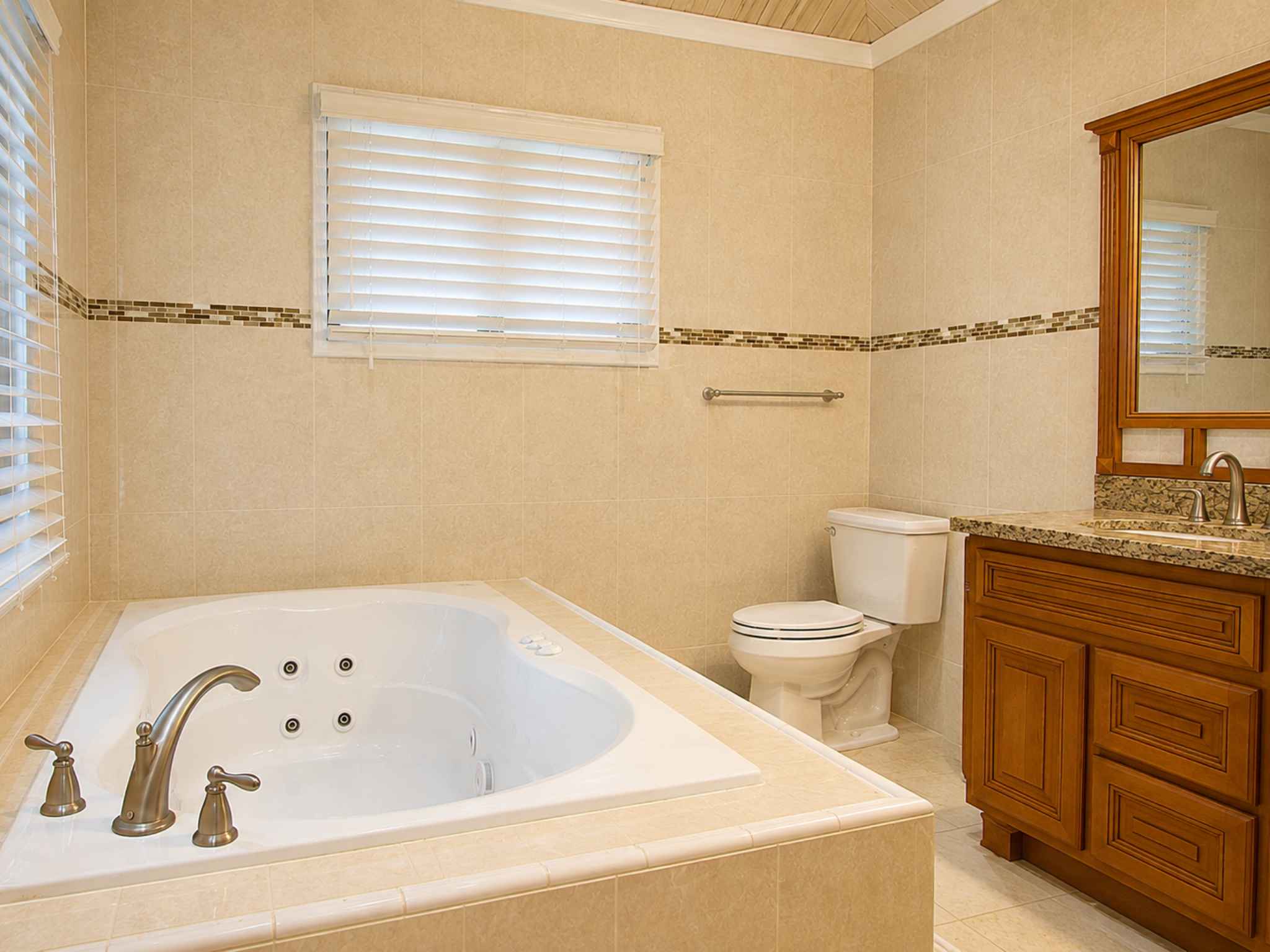 Primary bathroom with jetted tub, toilet, granite vanity and a mosaic tile border