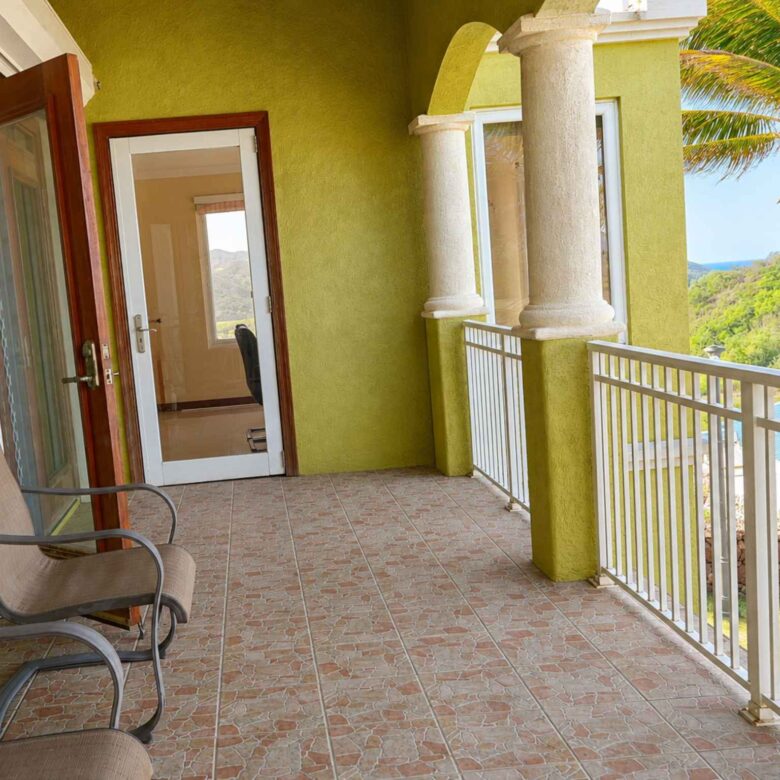 Tiled balcony with white railings and columns, overlooking palms and green hillside