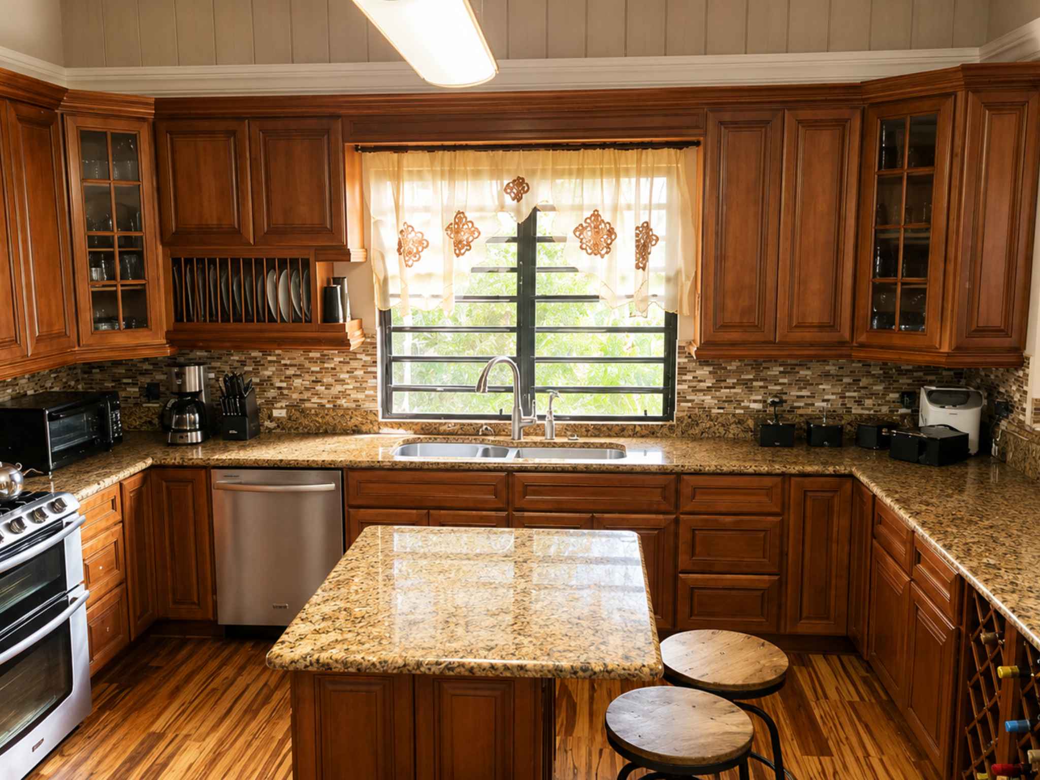 Kitchen with a double sink beneath a window, granite island, glass-front cabinets and plate storage