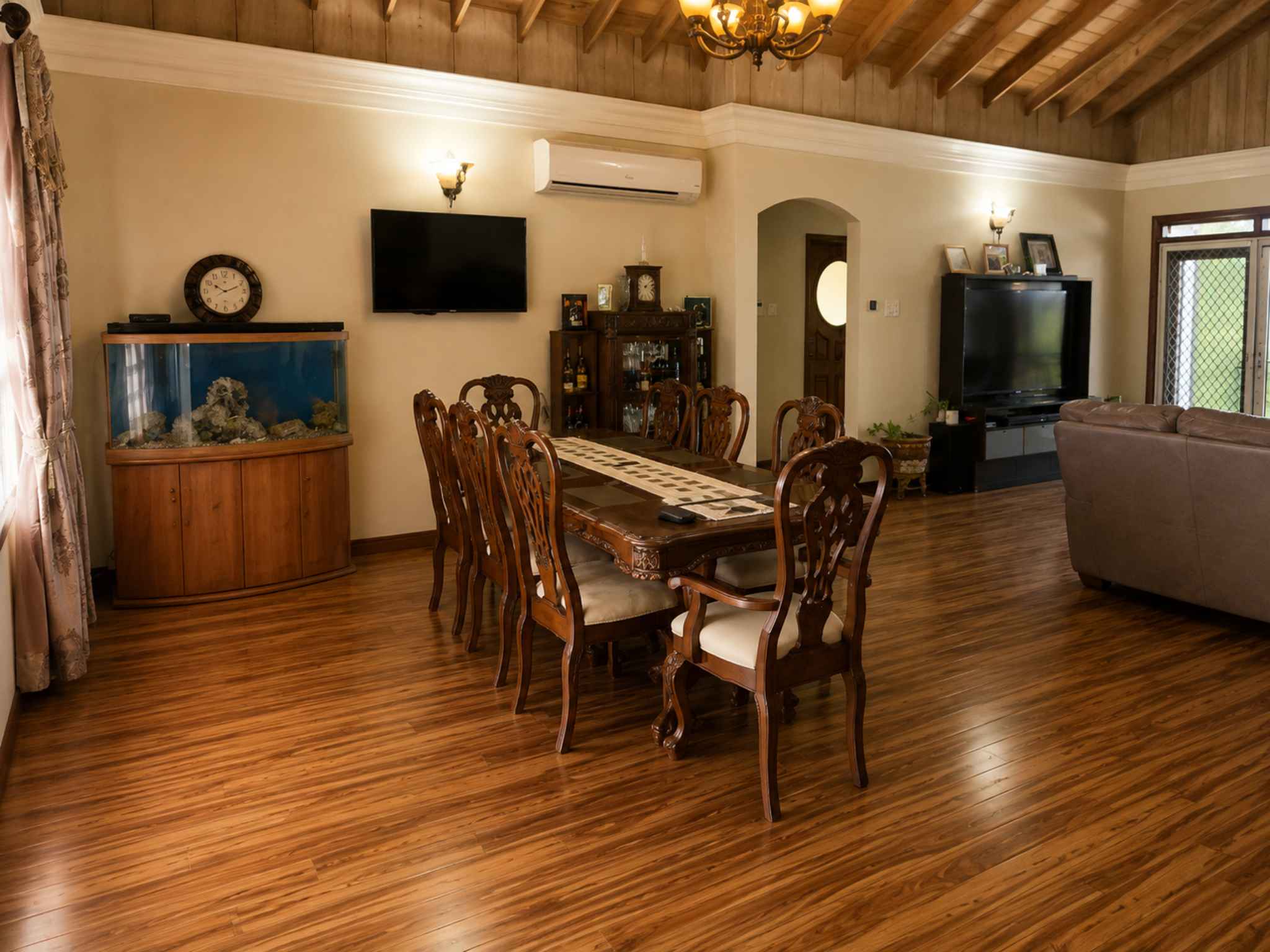 Dining area with a long timber table for eight beneath a chandelier and timber ceiling