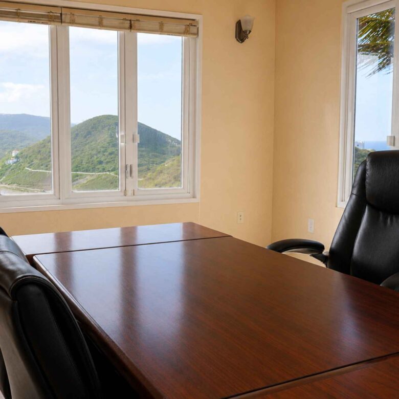 Executive office with a large desk and leather chairs, windows framing hillside and ocean views