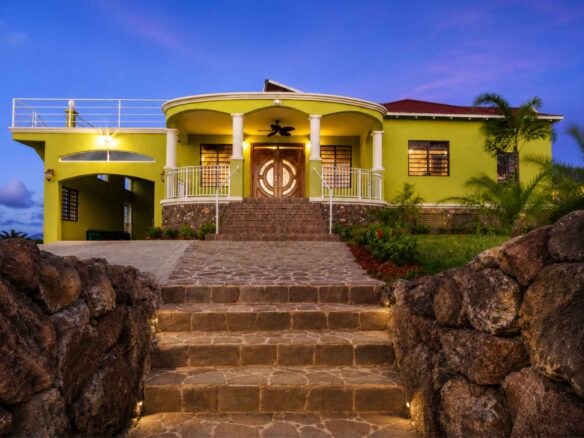Yellow hilltop villa lit at dusk, with stone steps rising to a columned entrance, Half Moon Bay, St Kitts