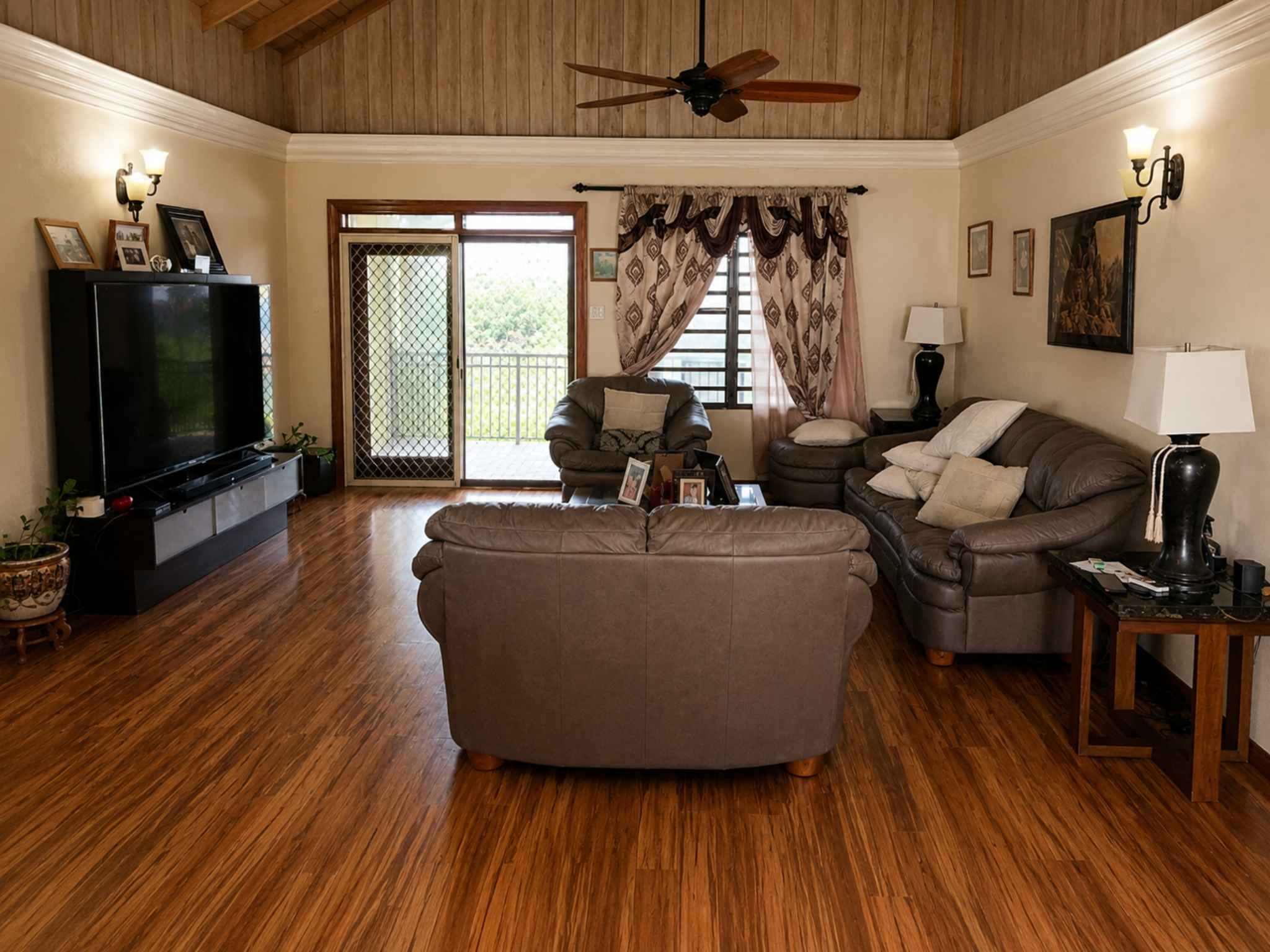 Living area with leather seating, ceiling fan, timber ceiling and doors to the balcony