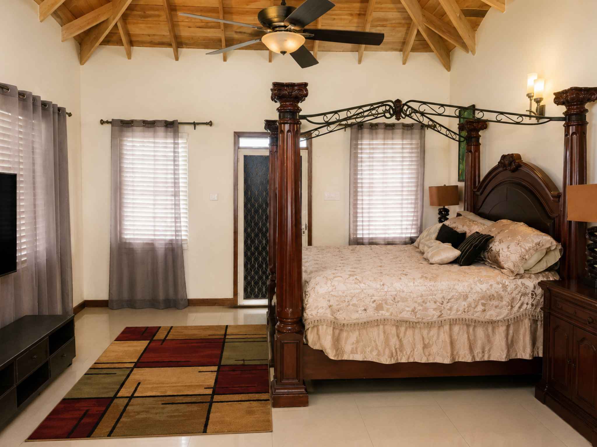 Primary bedroom with a carved four-poster bed, vaulted timber ceiling and tiled floor