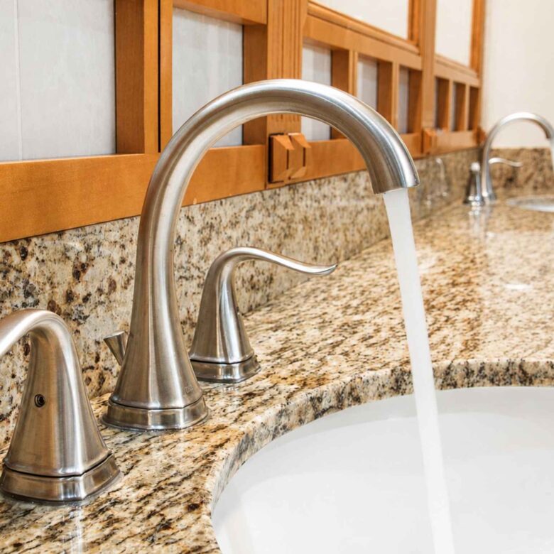 Brushed nickel faucet running water over a basin set in a granite vanity