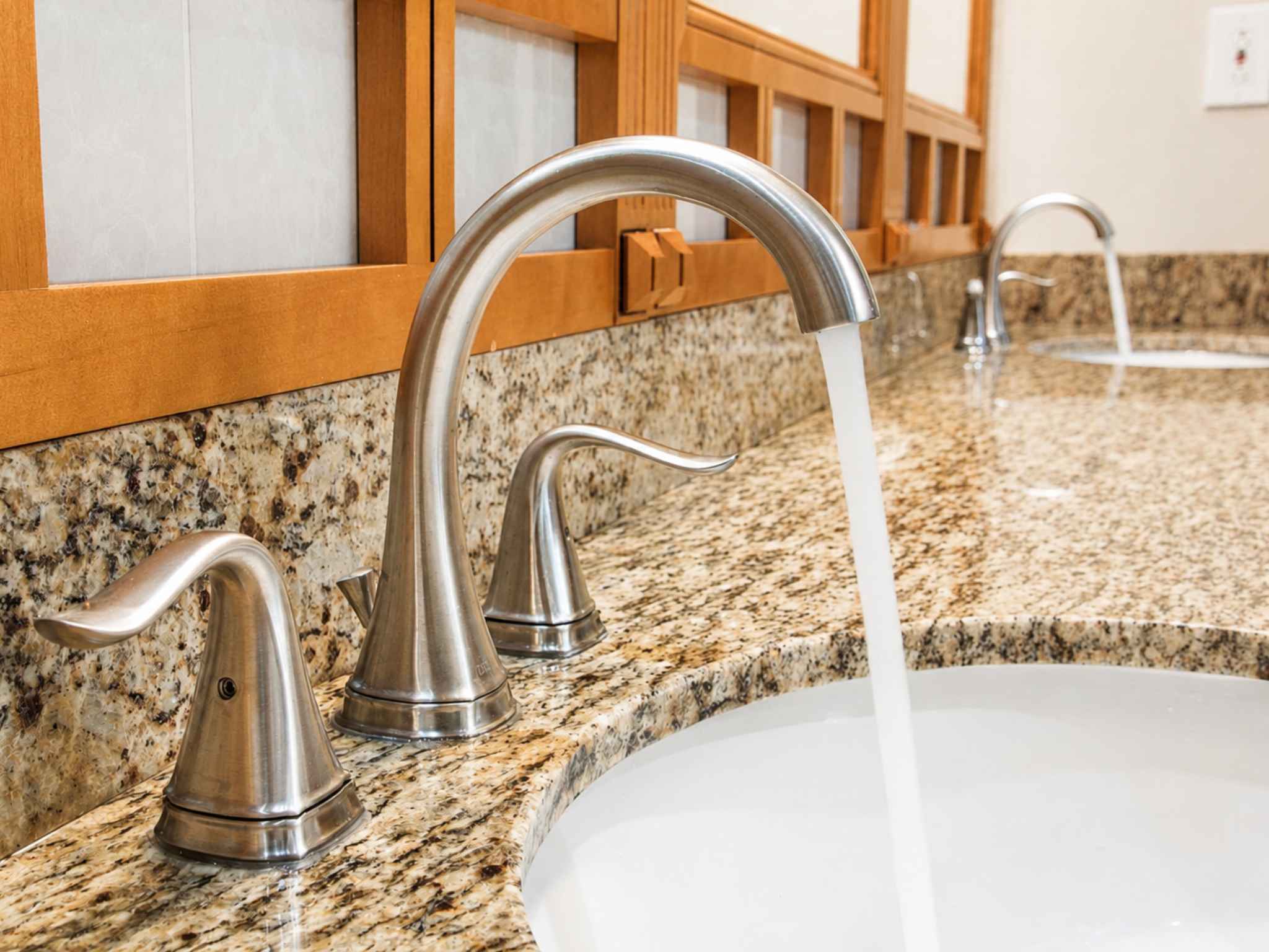 Brushed nickel faucet running water over a basin set in a granite vanity