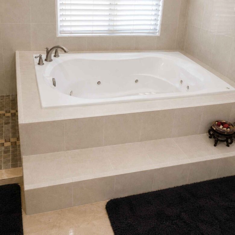White jetted soaking tub set into a tiled platform beside a window