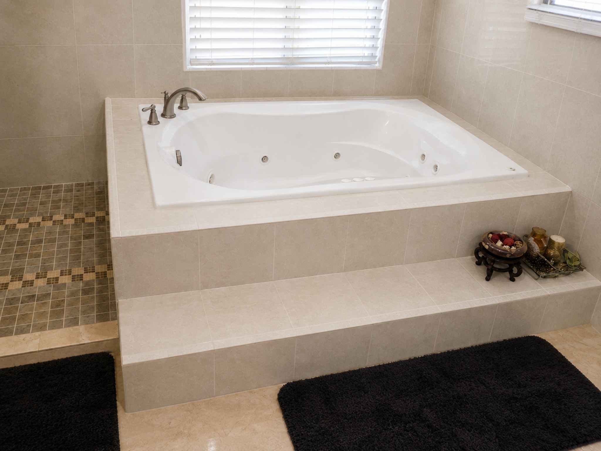 White jetted soaking tub set into a tiled platform beside a window