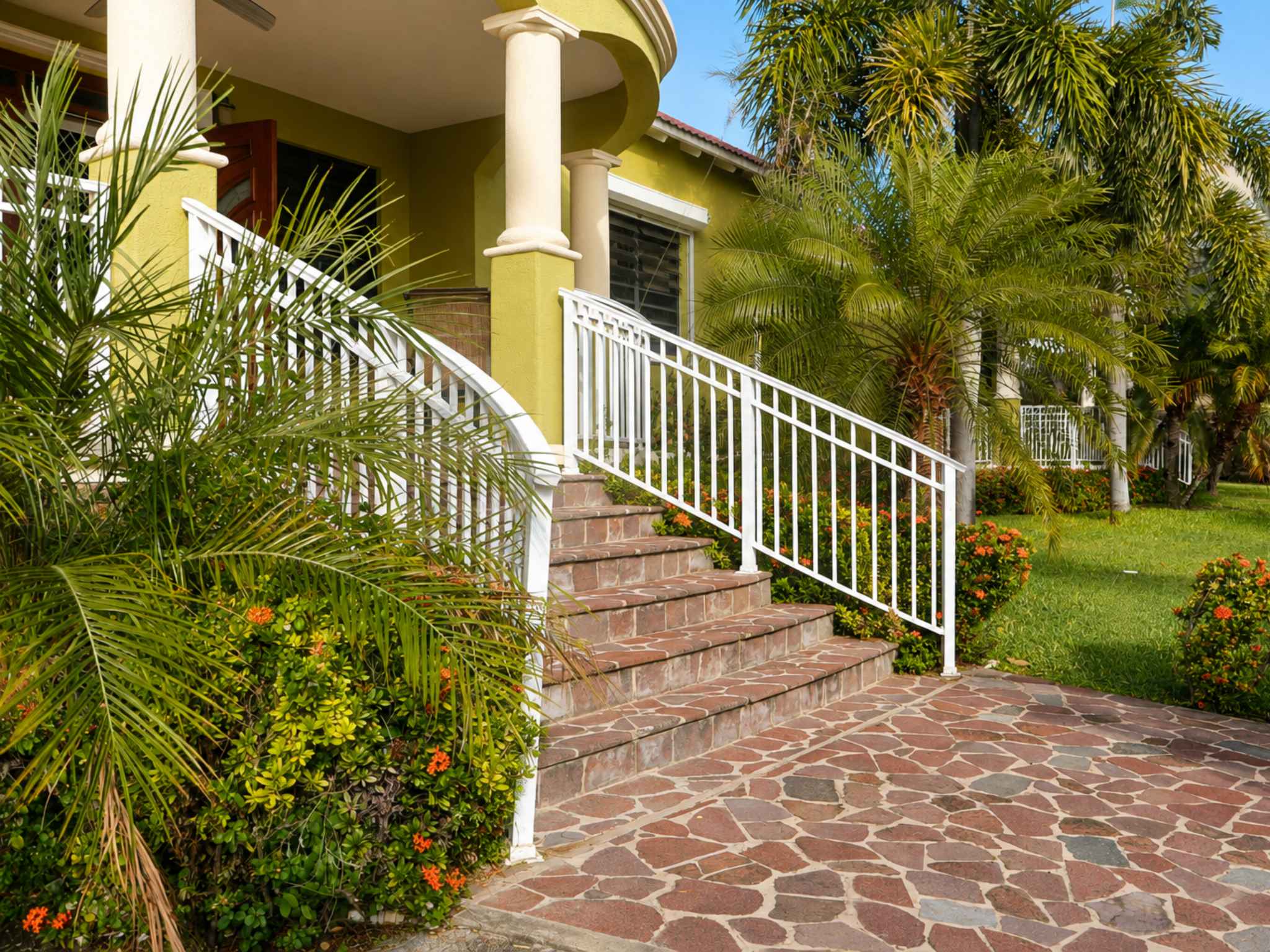 Stone-paved forecourt and tiled steps rising to the covered entrance between palms