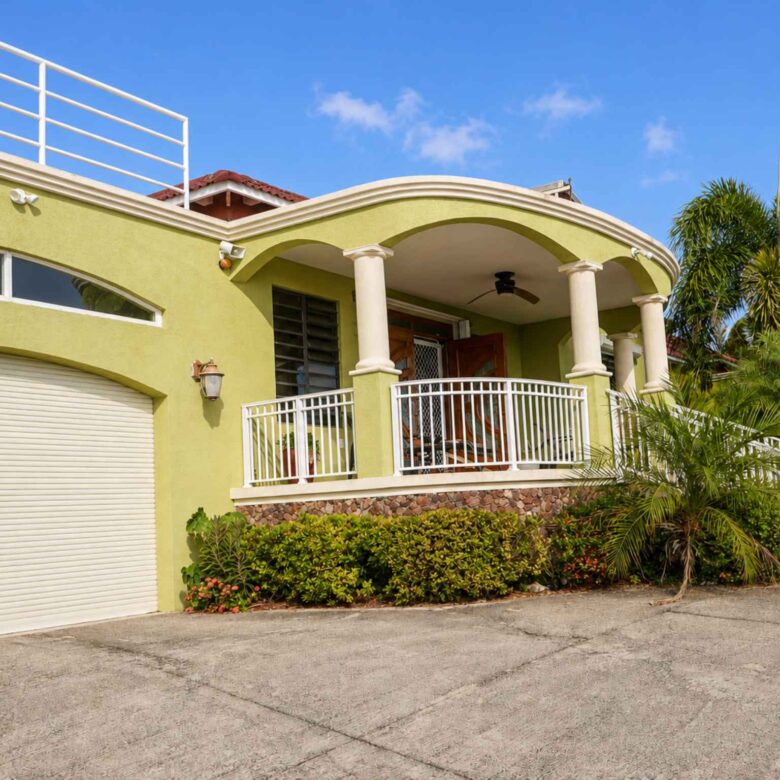 Garage door and covered columned entrance with white railings and tropical planting