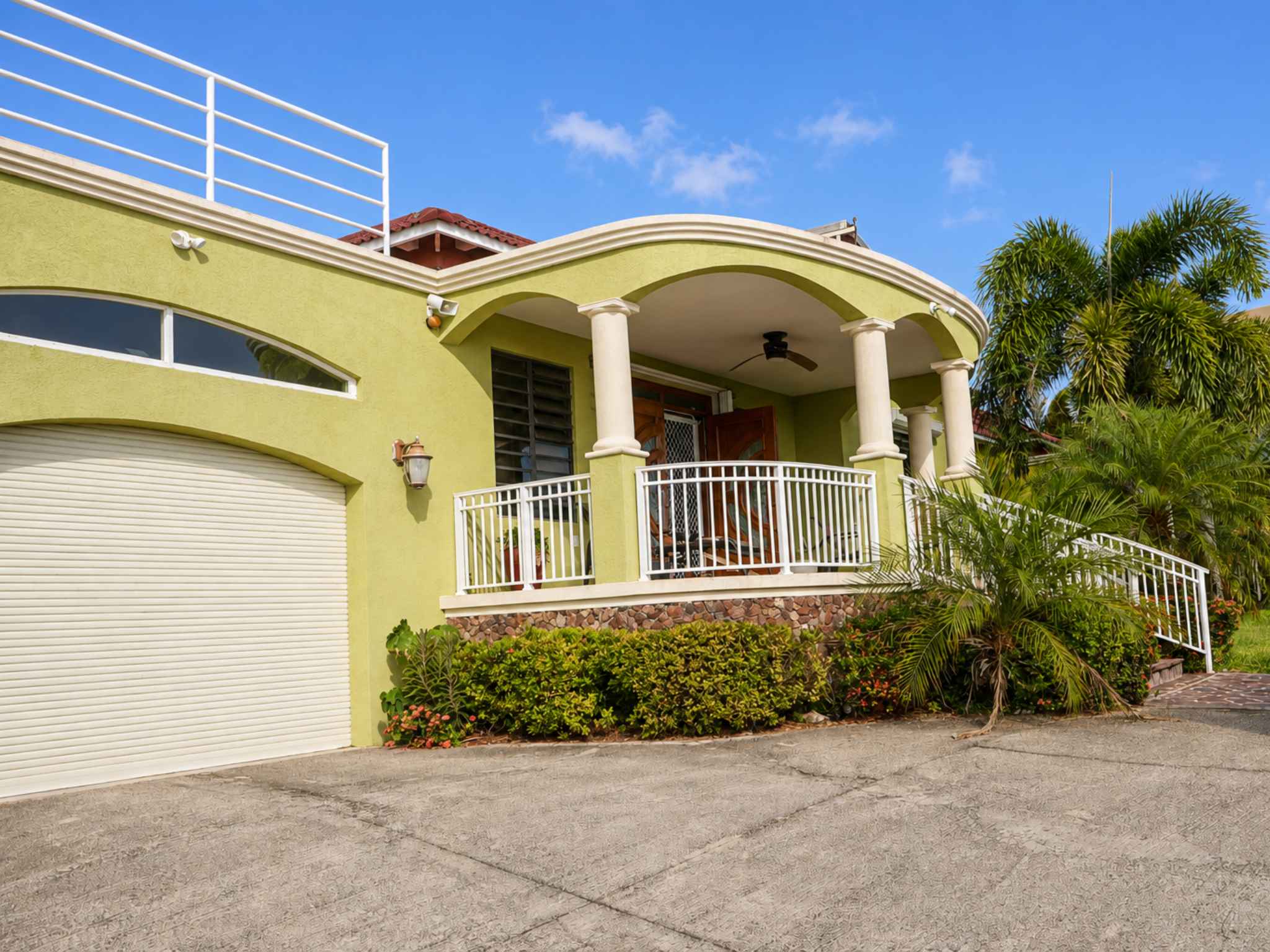 Garage door and covered columned entrance with white railings and tropical planting