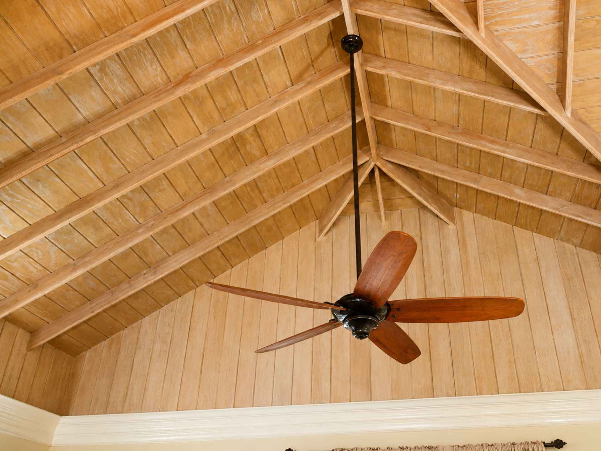 Detail of a vaulted timber ceiling with exposed rafters and a wooden ceiling fan