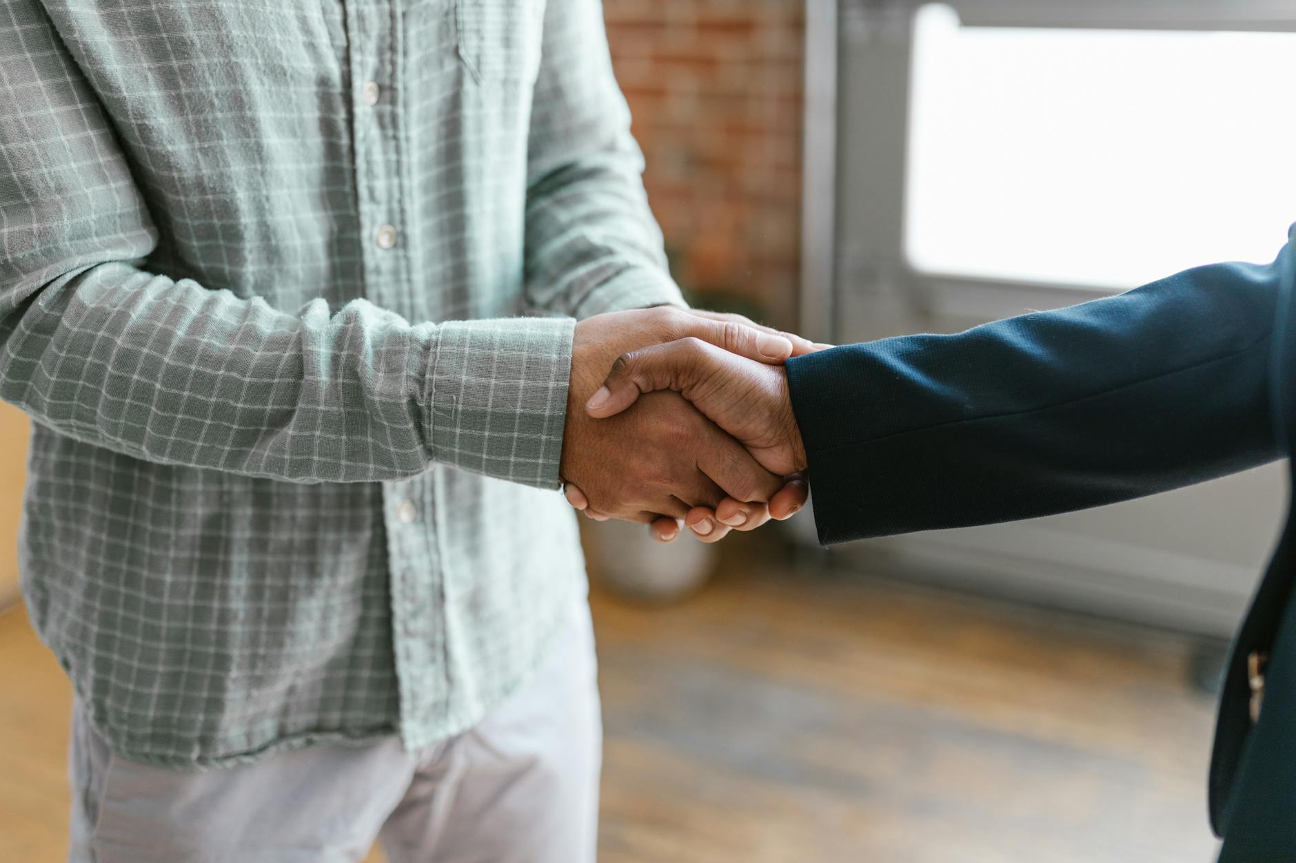 a person in green plaid long sleeve shirt shaking hands with person in black blazer